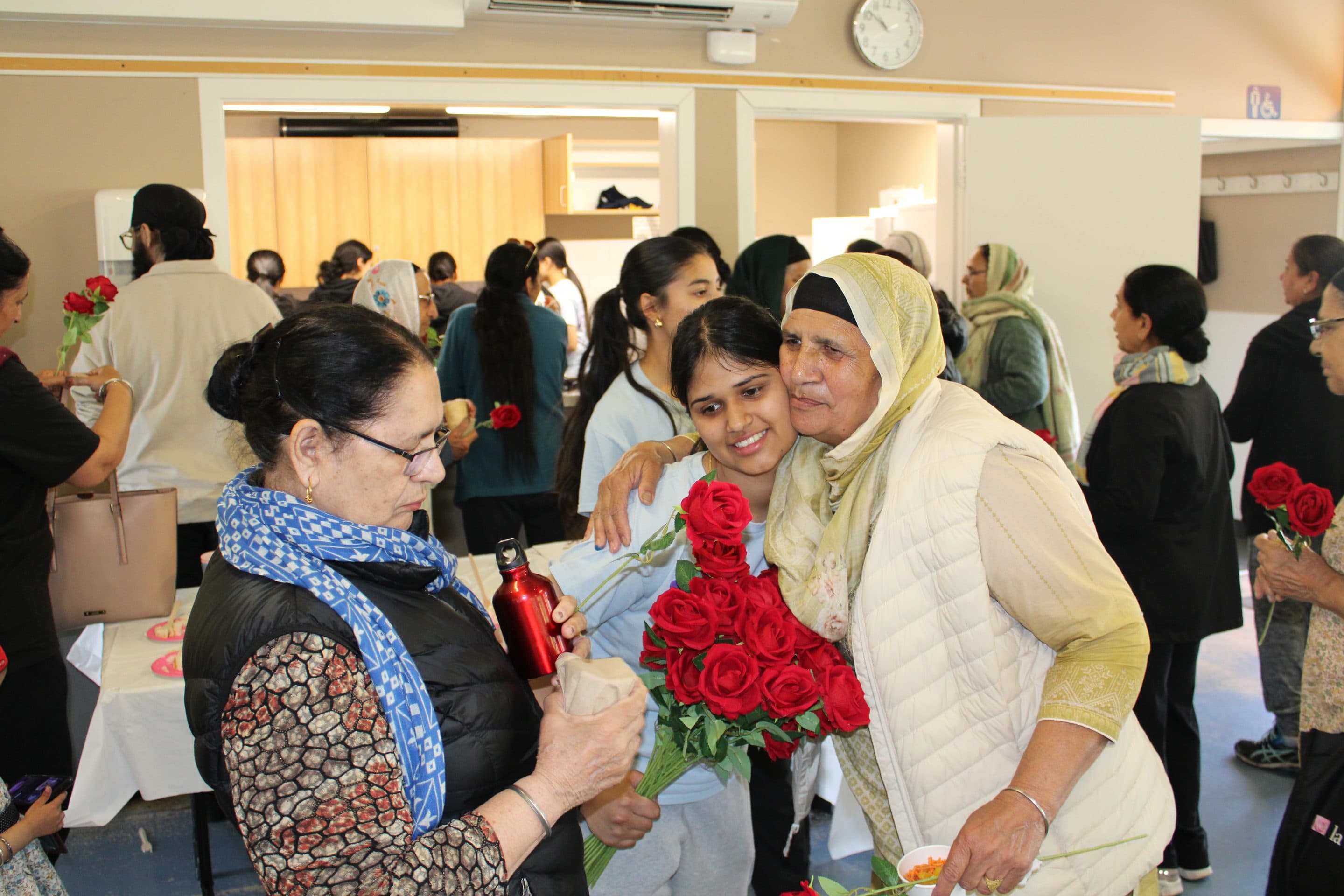 An older woman embracing a younger volunteer; both hold red roses.