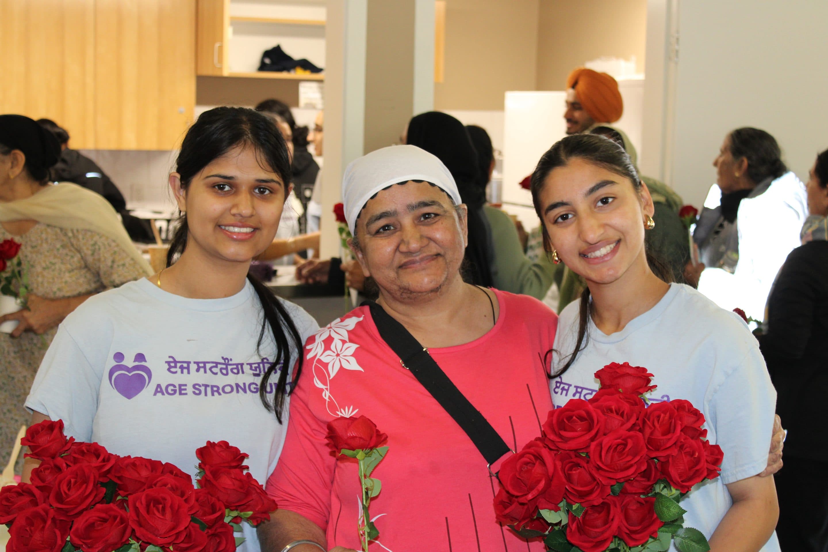 Two volunteers in Age Strong shirts with a matriarch between them.