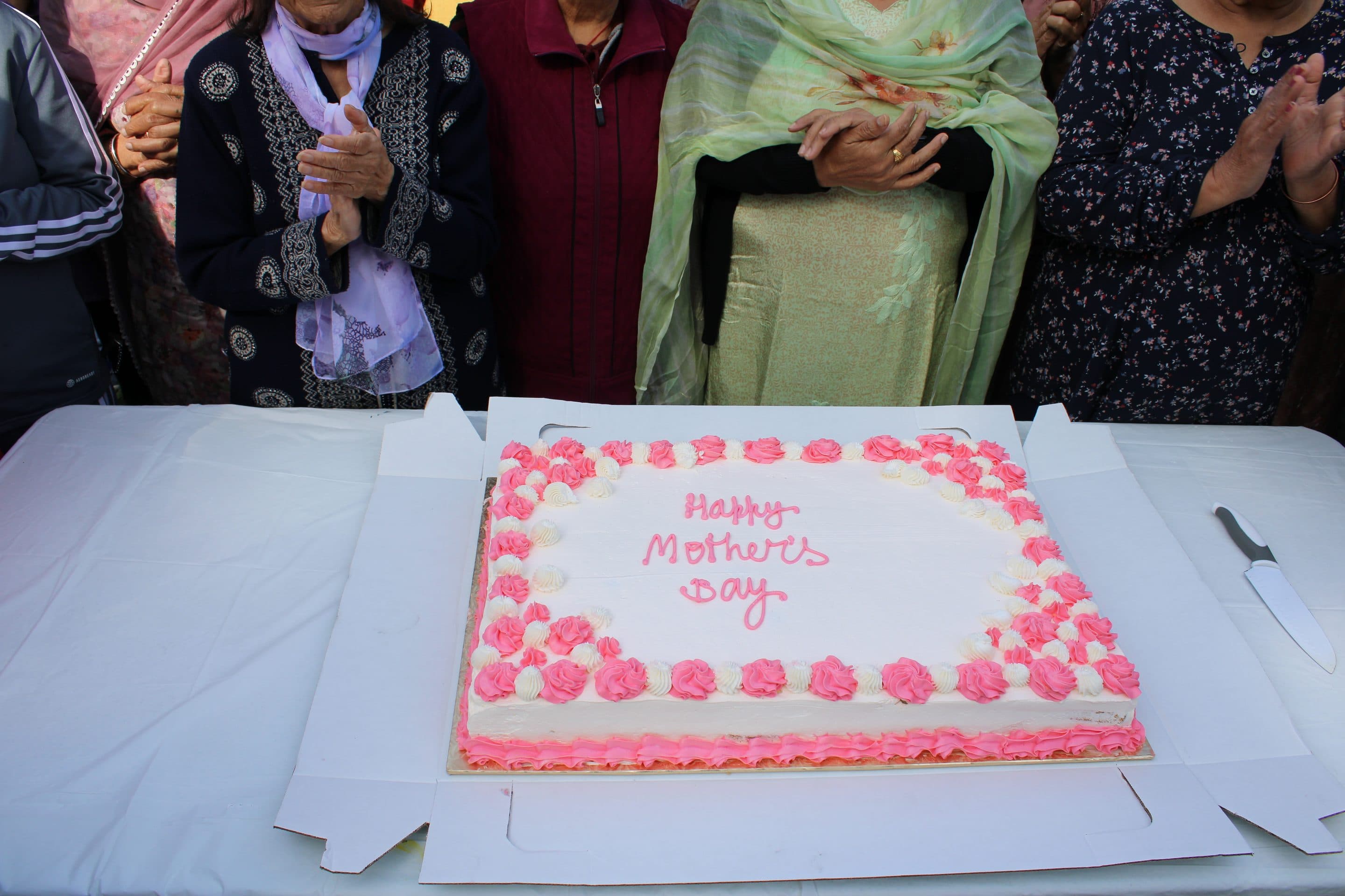 Hands gathered around a pink-iced Happy Mother's Day cake.