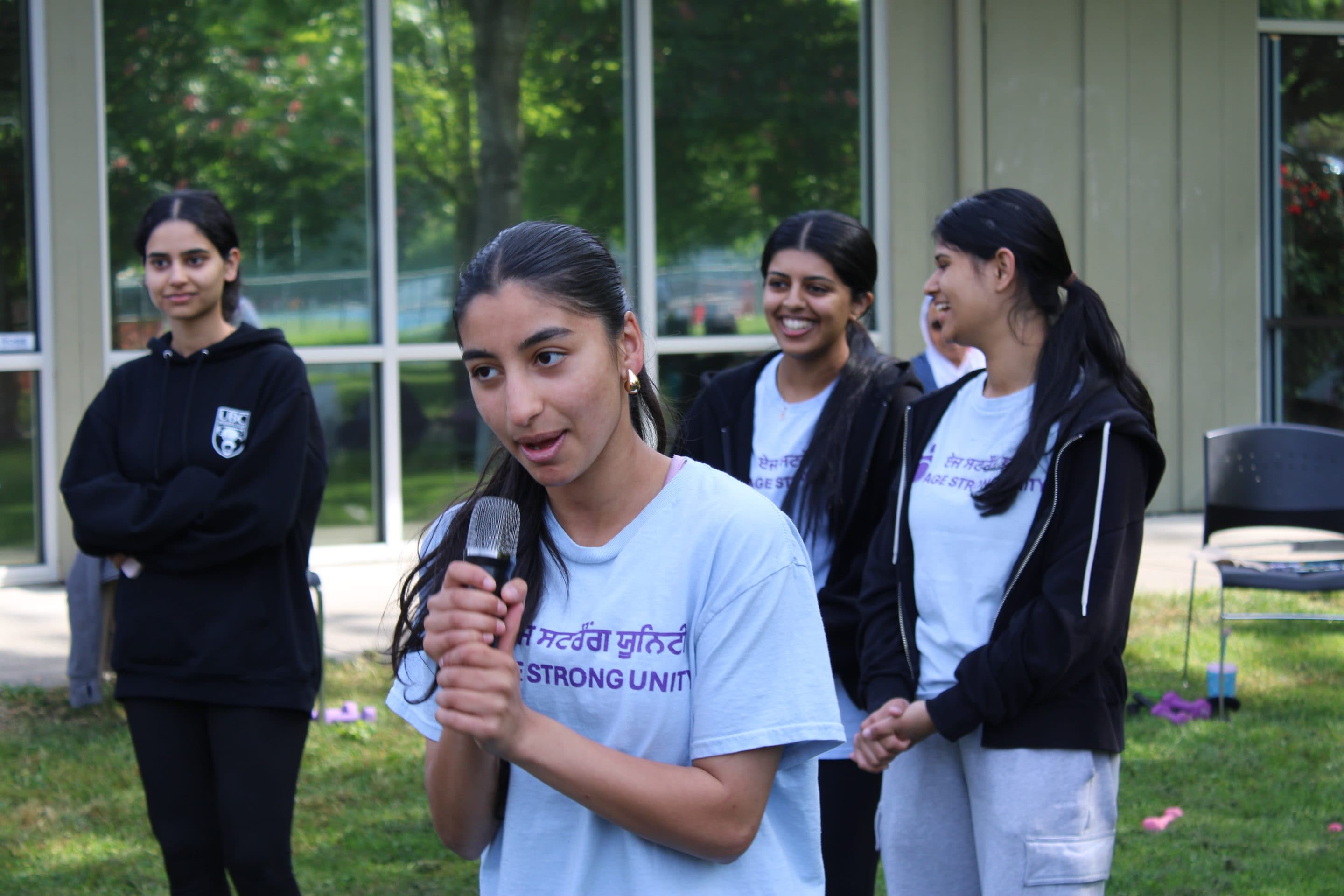 A young volunteer speaking, with three friends laughing softly behind her.