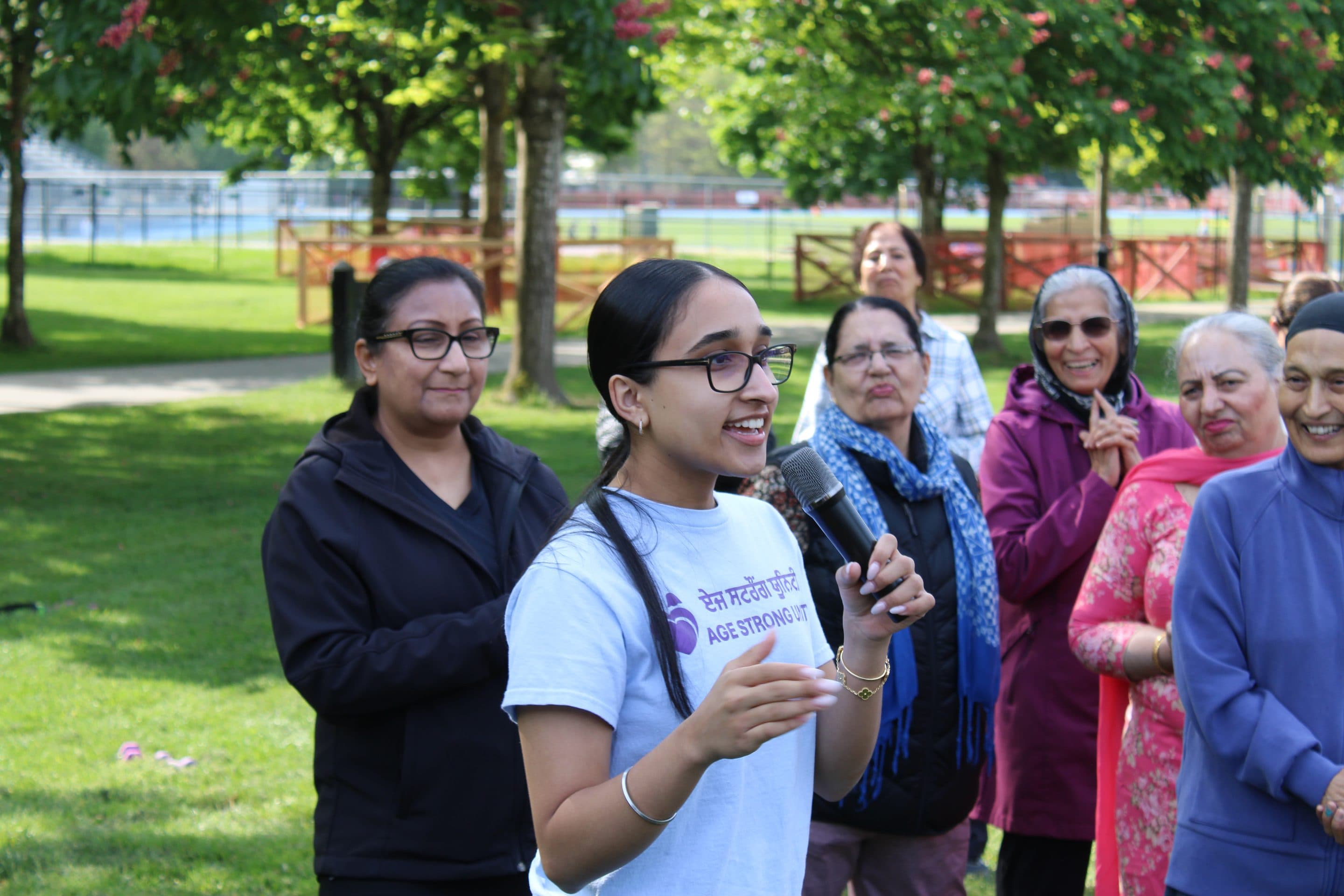 A young volunteer addressing the gathering, older women smiling behind.