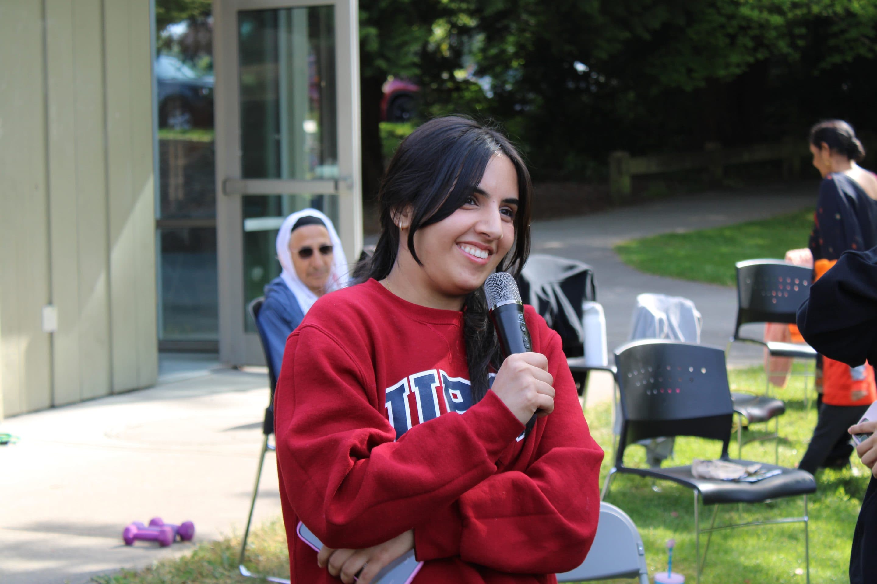 A volunteer in a red sweatshirt smiling mid-speech, microphone in hand.