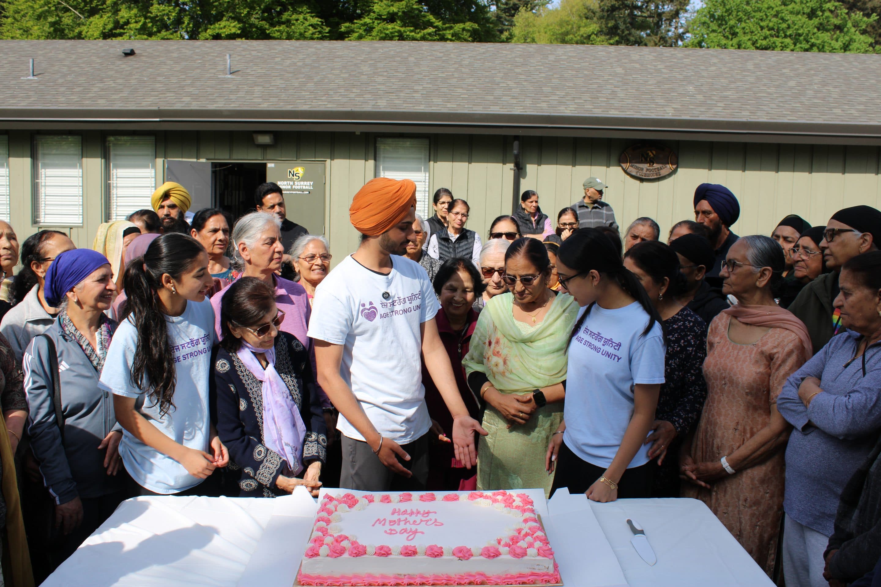 A wide view of the cake-cutting moment, surrounded by mothers and volunteers.