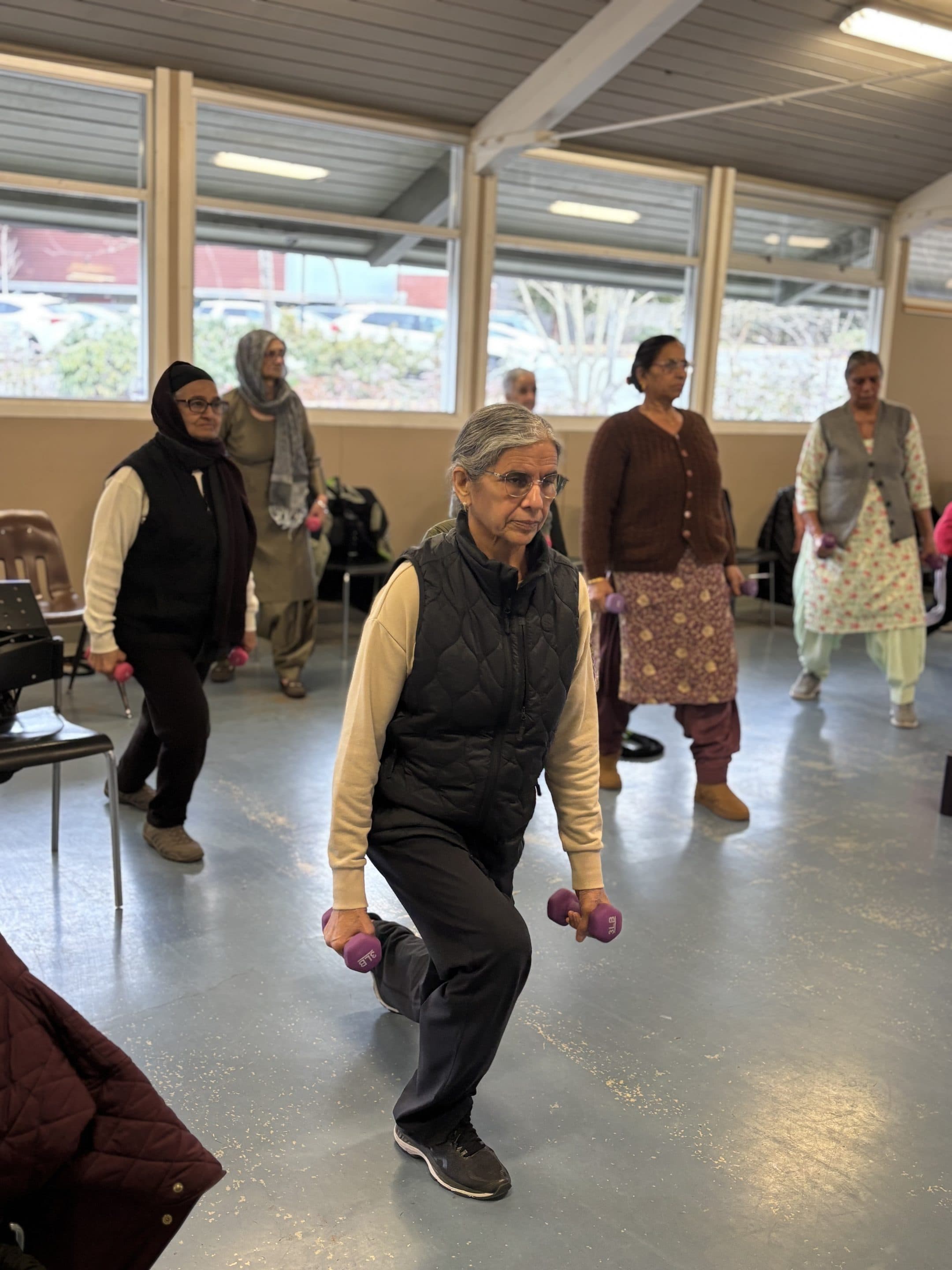 An older woman in a strength class, focused on lifting a small dumbbell.
