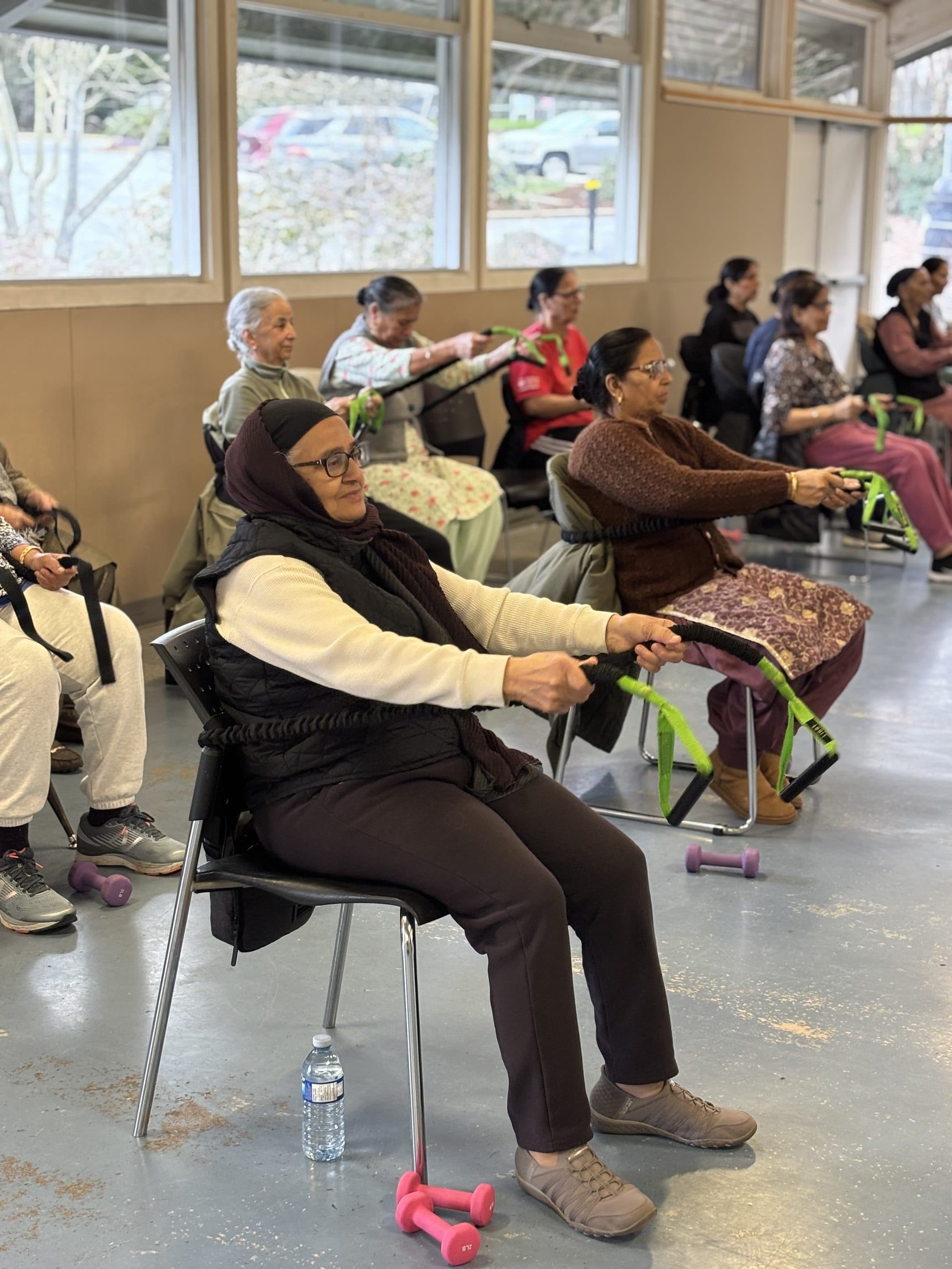 An older woman seated and pulling on a green resistance band.
