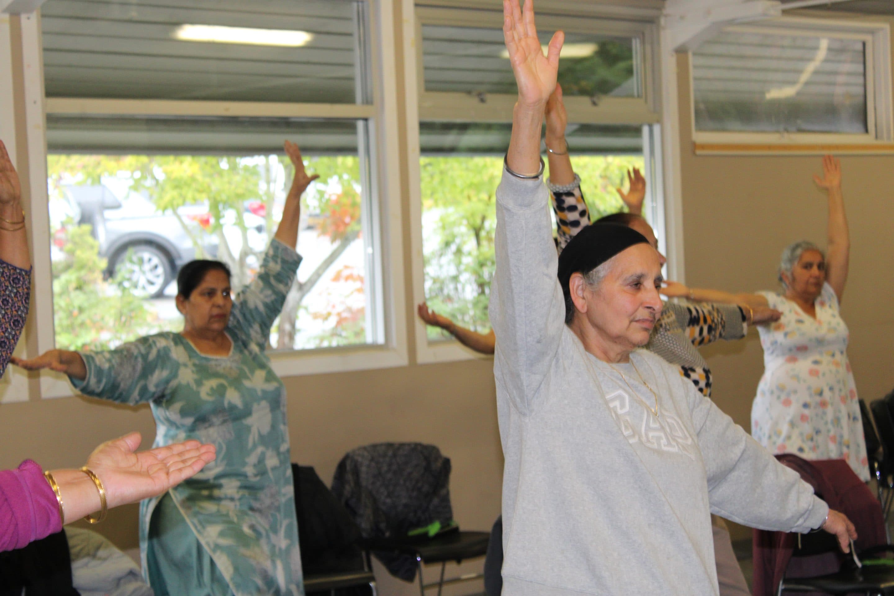 A class of older adults raising their arms overhead in unison.